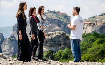 Guide explaining Meteora's history to a group with mountains in the background.