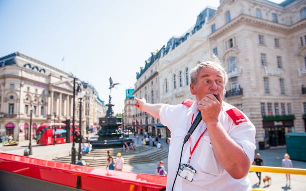 Tour guide speaking on Tootbus in front of Eros statue at Piccadilly Circus, London.