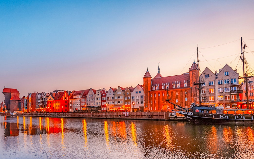 Gdansk waterfront with historic buildings and ship at sunset.