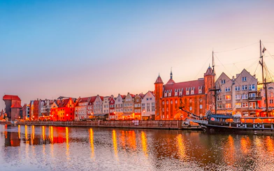 Gdansk waterfront with historic buildings and ship at sunset.