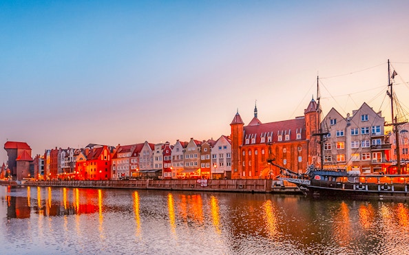 Gdansk waterfront with historic buildings and ship at sunset.