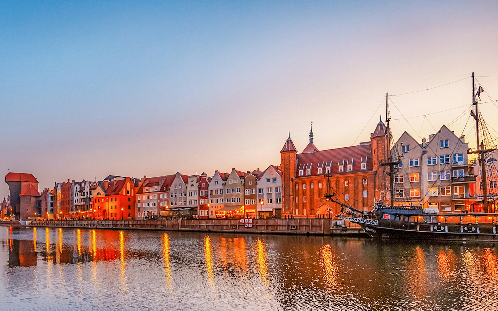 Gdansk waterfront with historic buildings and ship at sunset.