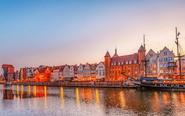 Gdansk waterfront with historic buildings and ship at sunset.