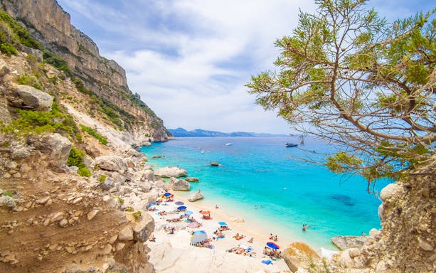 Guided trekking group at Cala Goloritzè beach, Sardinia, with turquoise sea and rocky cliffs.