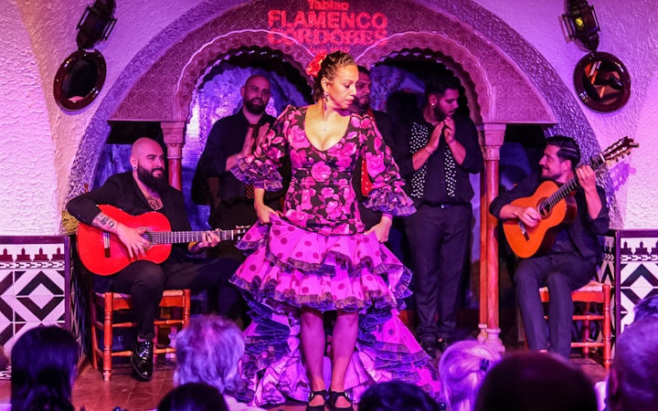 Flamenco dancer performing at Tablao Cordobes with musicians playing guitar in the background.