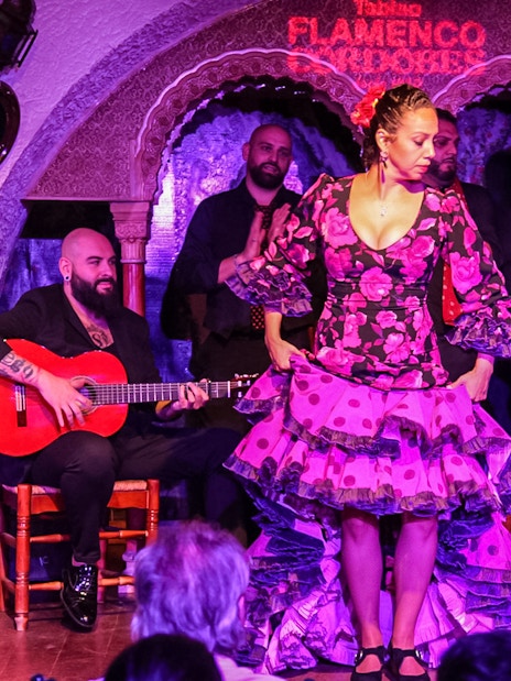Flamenco dancer performing at Tablao Cordobes with musicians playing guitar in the background.