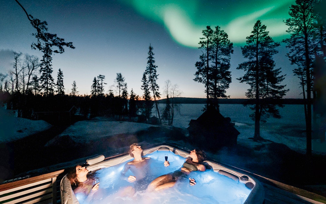 Guests relaxing in a hot tub under Northern Lights in Rovaniemi.