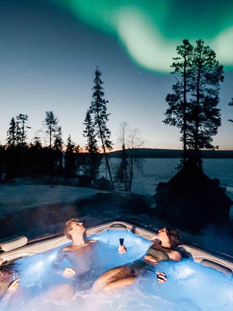 Guests relaxing in a hot tub under Northern Lights in Rovaniemi.