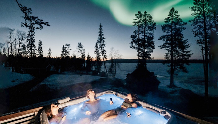 Guests relaxing in a hot tub under Northern Lights in Rovaniemi.