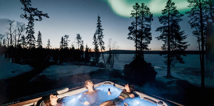 Guests relaxing in a hot tub under Northern Lights in Rovaniemi.