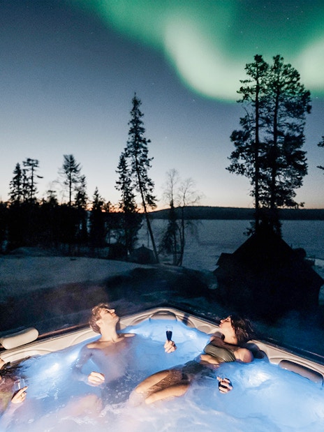Guests relaxing in a hot tub under Northern Lights in Rovaniemi.