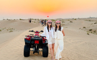 Two people standing beside an ATV in the Abu Dhabi desert at sunset during an evening safari tour.
