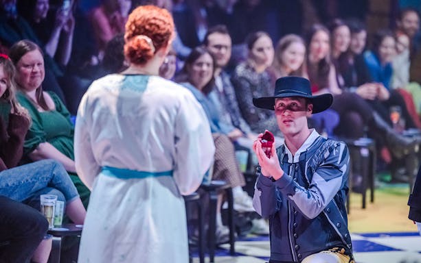 Man in costume kneeling with ring box during Plied and Prejudice performance.
