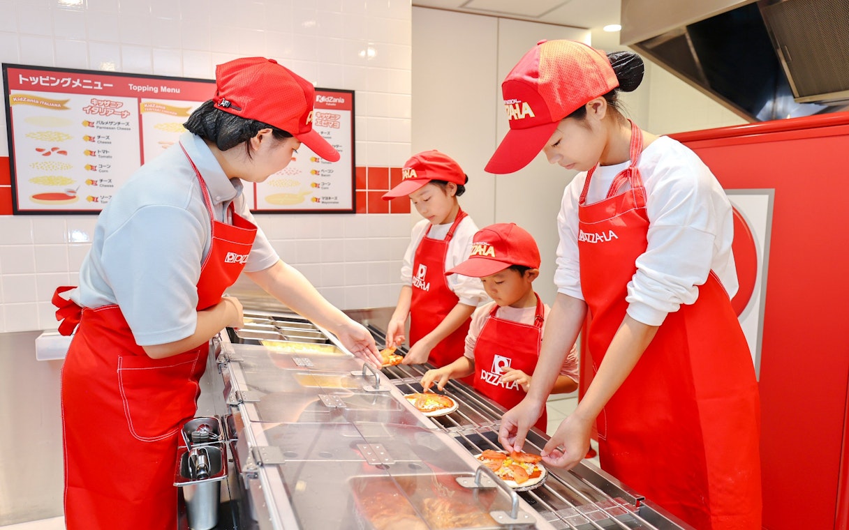 Children making pizzas at KidZania Fukuoka pizzeria.