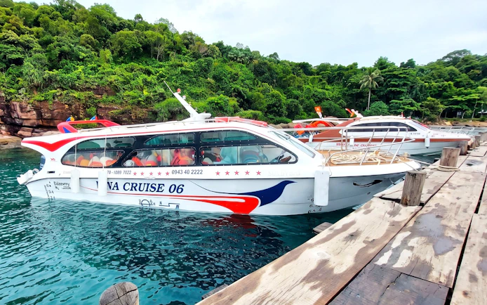 Speedboat docked at a wooden pier with lush green forest in the background.
