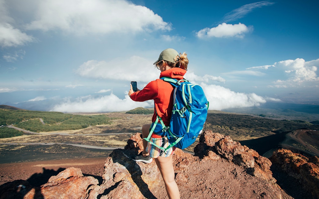 Person taking a photo on Mount Etna, Sicily, with a view of volcanic landscape.