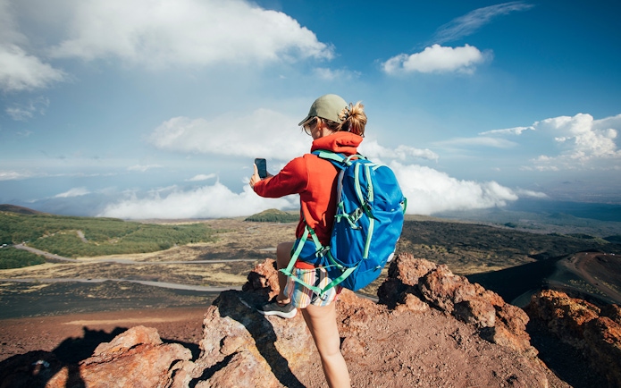 Person taking a photo on Mount Etna, Sicily, with a view of volcanic landscape.