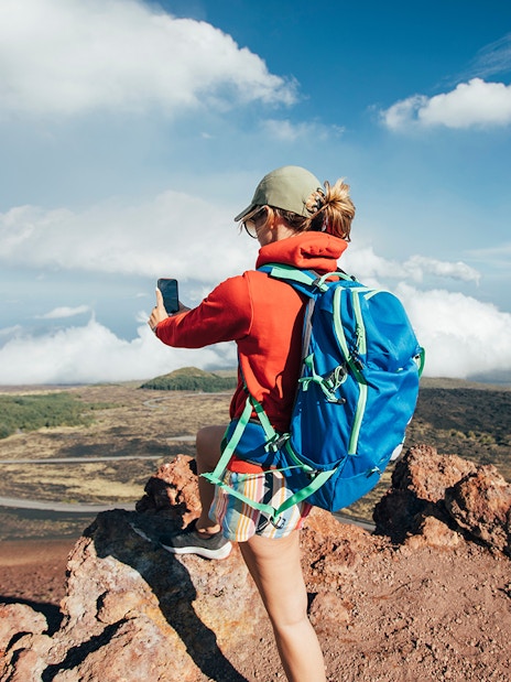 Person taking a photo on Mount Etna, Sicily, with a view of volcanic landscape.