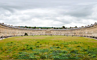 Royal Crescent in Bath, showcasing Georgian architecture with a grassy foreground.