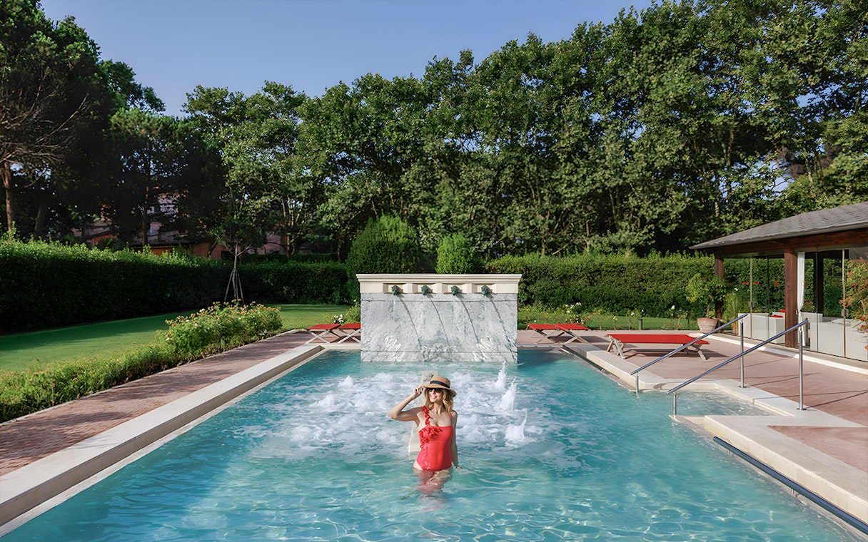 Visitor enjoying the pool at QC Terme Roma Resort & Spa, Italy, surrounded by greenery.