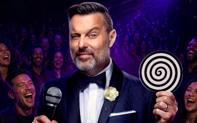 Hypnotist performing on stage with audience laughing, holding a spiral disc.
