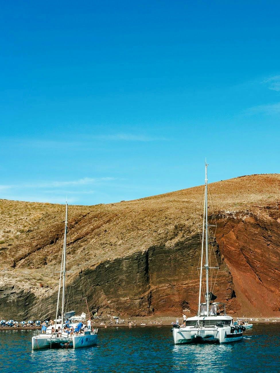 Catamaran cruise near the red beach cliffs in Santorini.