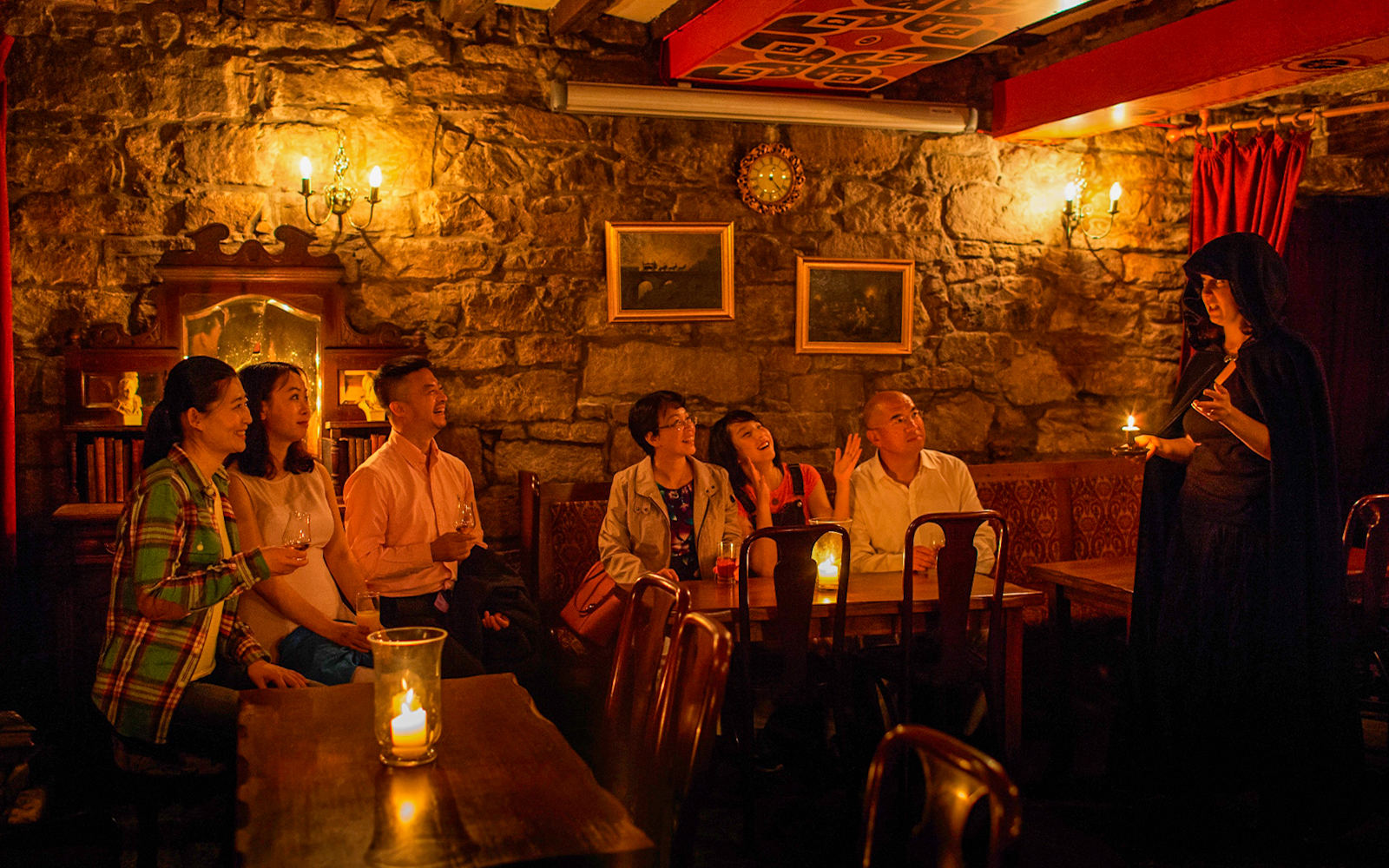 Group listening to a storyteller in a dimly lit Edinburgh pub during ghost tour.
