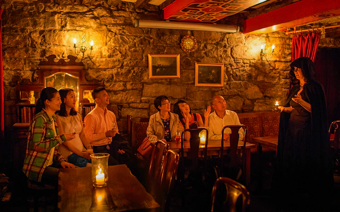 Group listening to a storyteller in a dimly lit Edinburgh pub during ghost tour.
