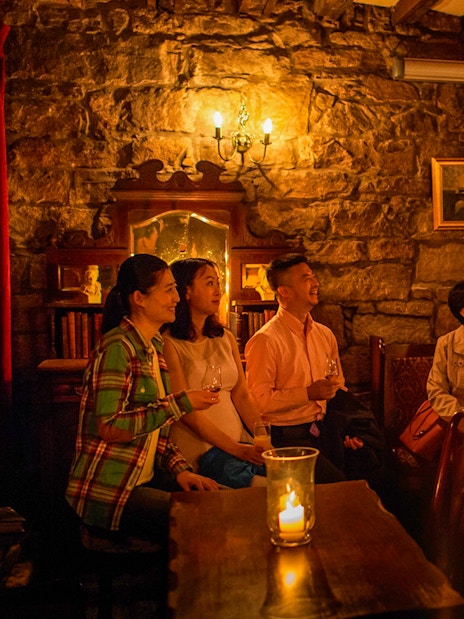 Group listening to a storyteller in a dimly lit Edinburgh pub during ghost tour.
