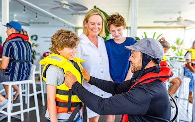 Crew member assists child with life vest before Gold Coast jet boat ride.