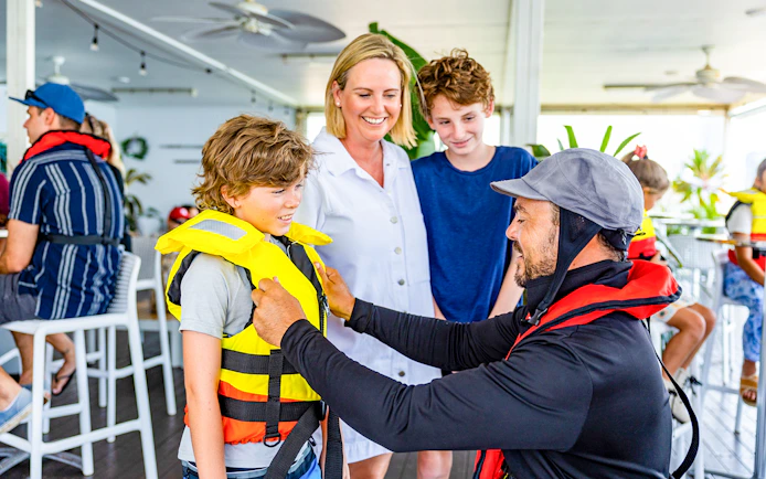 Crew member assists child with life vest before Gold Coast jet boat ride.