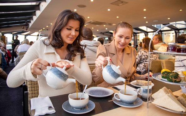 Guests enjoying afternoon tea on a Thames River cruise with sandwiches and pastries.