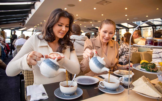 Guests enjoying afternoon tea on a Thames River cruise with sandwiches and pastries.