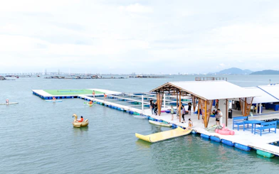 Catamaran dock with people enjoying water activities in Penang, with distant city skyline.