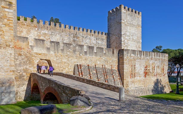 St. George Castle entrance with visitors on a stone bridge, Lisbon, Portugal.