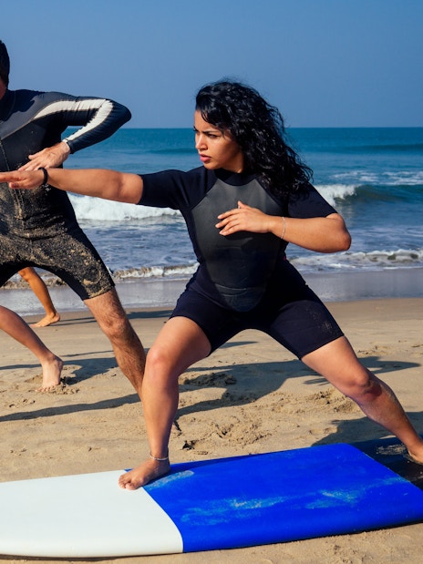 Surf instructor with two beginner surfers practicing balance on the beach in Lisbon.