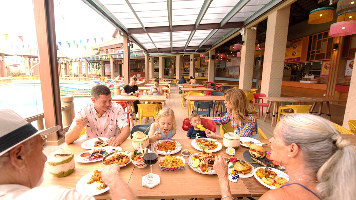 Family dining at a colorful outdoor restaurant in a tropical setting.