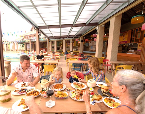 Family dining at a colorful outdoor restaurant in a tropical setting.