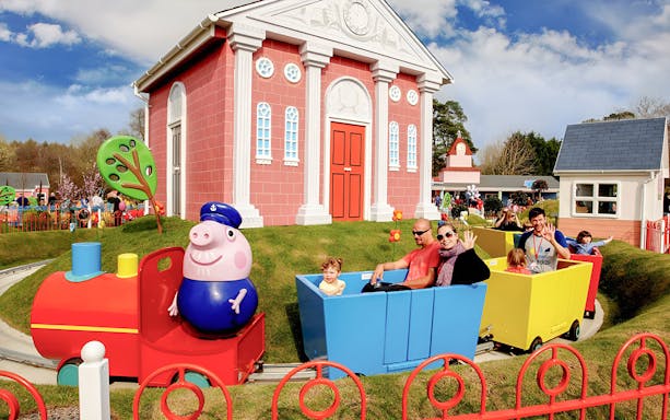 Visitors riding Peppa Pig train at Paultons Park, featuring colorful buildings and attractions.