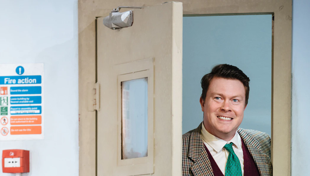 Man smiling while standing in a doorway, related to "Accidental Death of an Anarchist" tickets.