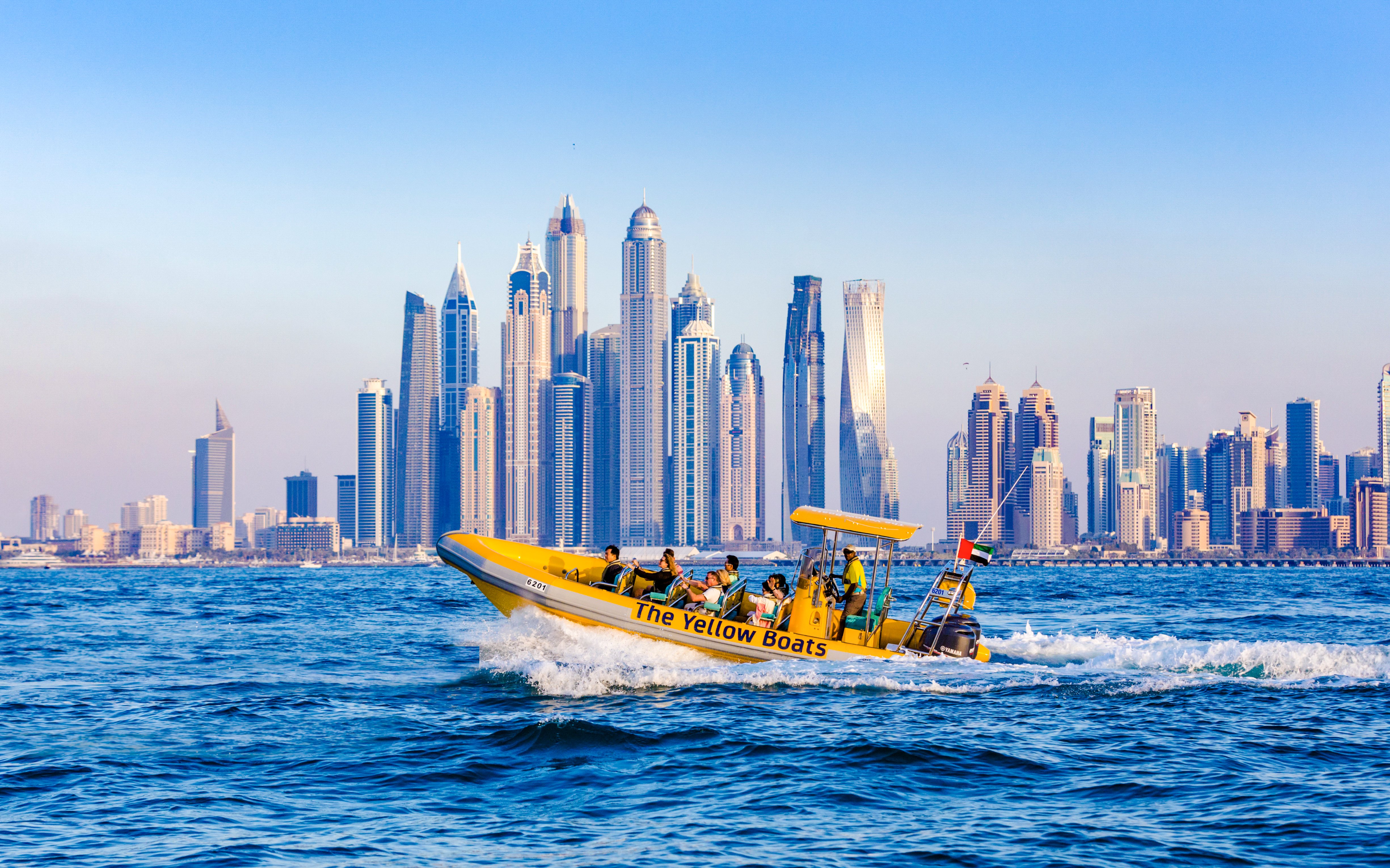 Yellow boat cruising near Dubai skyline with skyscrapers in the background.