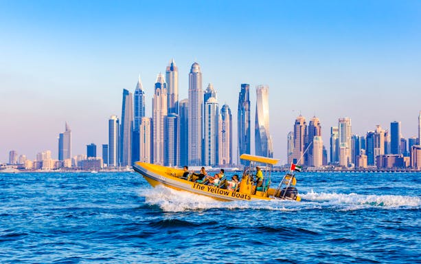 Yellow boat cruising near Dubai skyline with skyscrapers in the background.