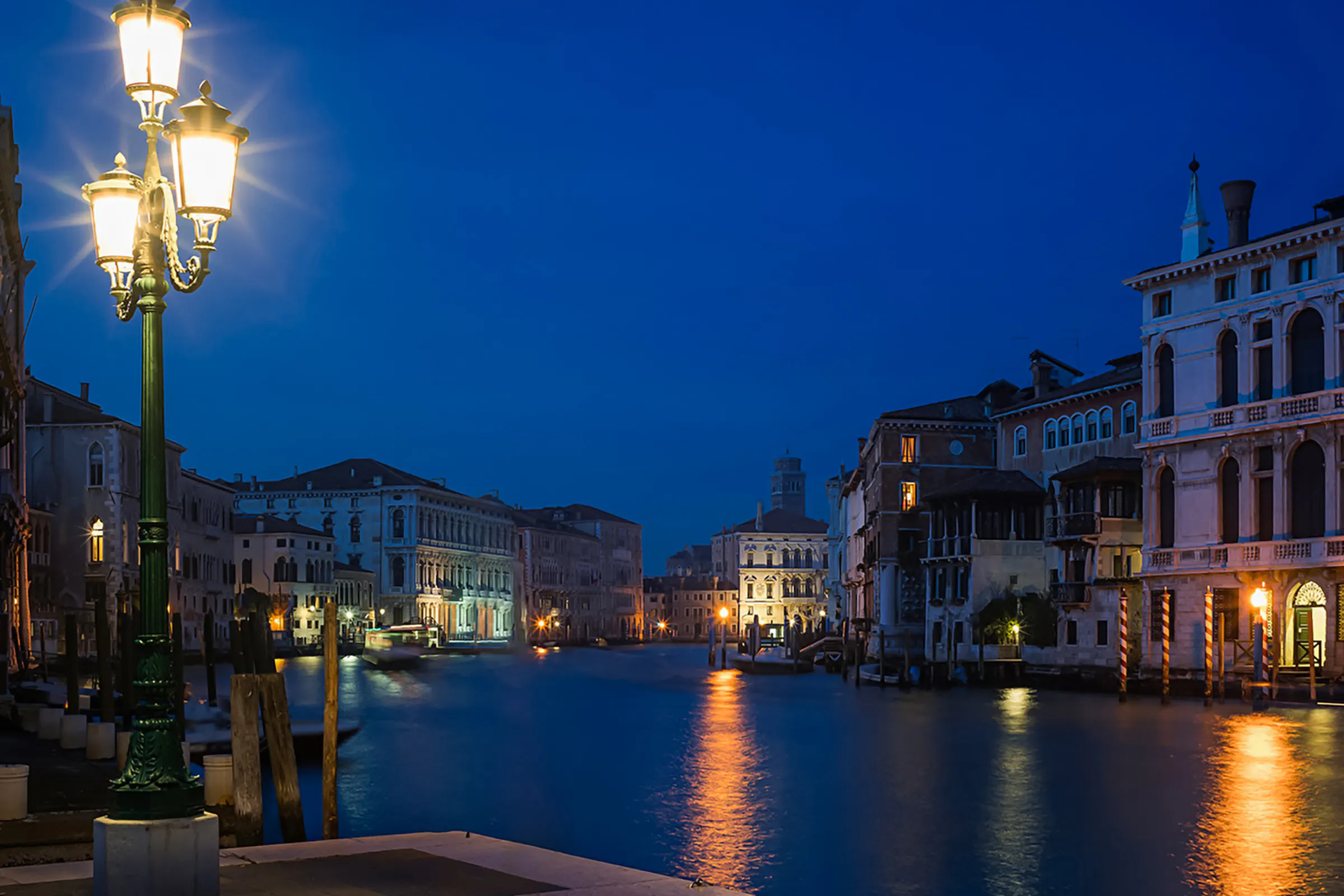 Venice canal at night with illuminated buildings and street lamps, setting for ghost tour.