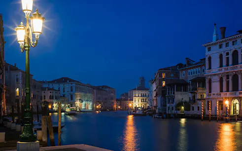 Venice canal at night with illuminated buildings and street lamps, setting for ghost tour.