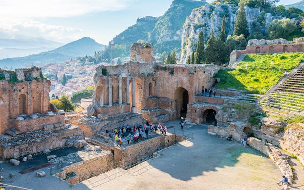 Visitors exploring Taormina Ancient Theatre with scenic hillside views.