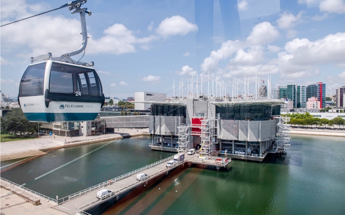 Lisbon Oceanarium with Telecabine cable car over water, cityscape in background.