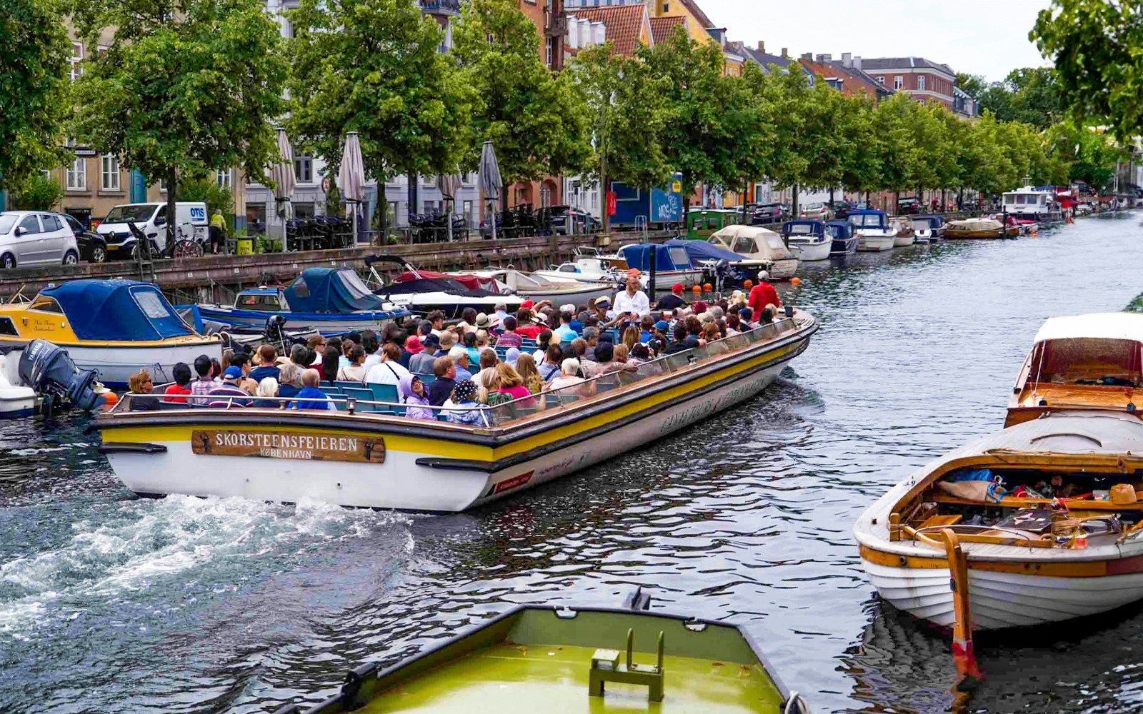 Copenhagen canal tour with people on a boat passing colorful waterfront buildings.