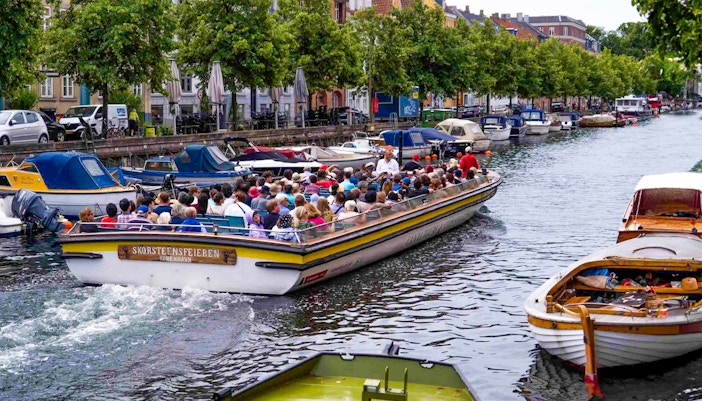 Copenhagen canal tour with people on a boat passing colorful waterfront buildings.
