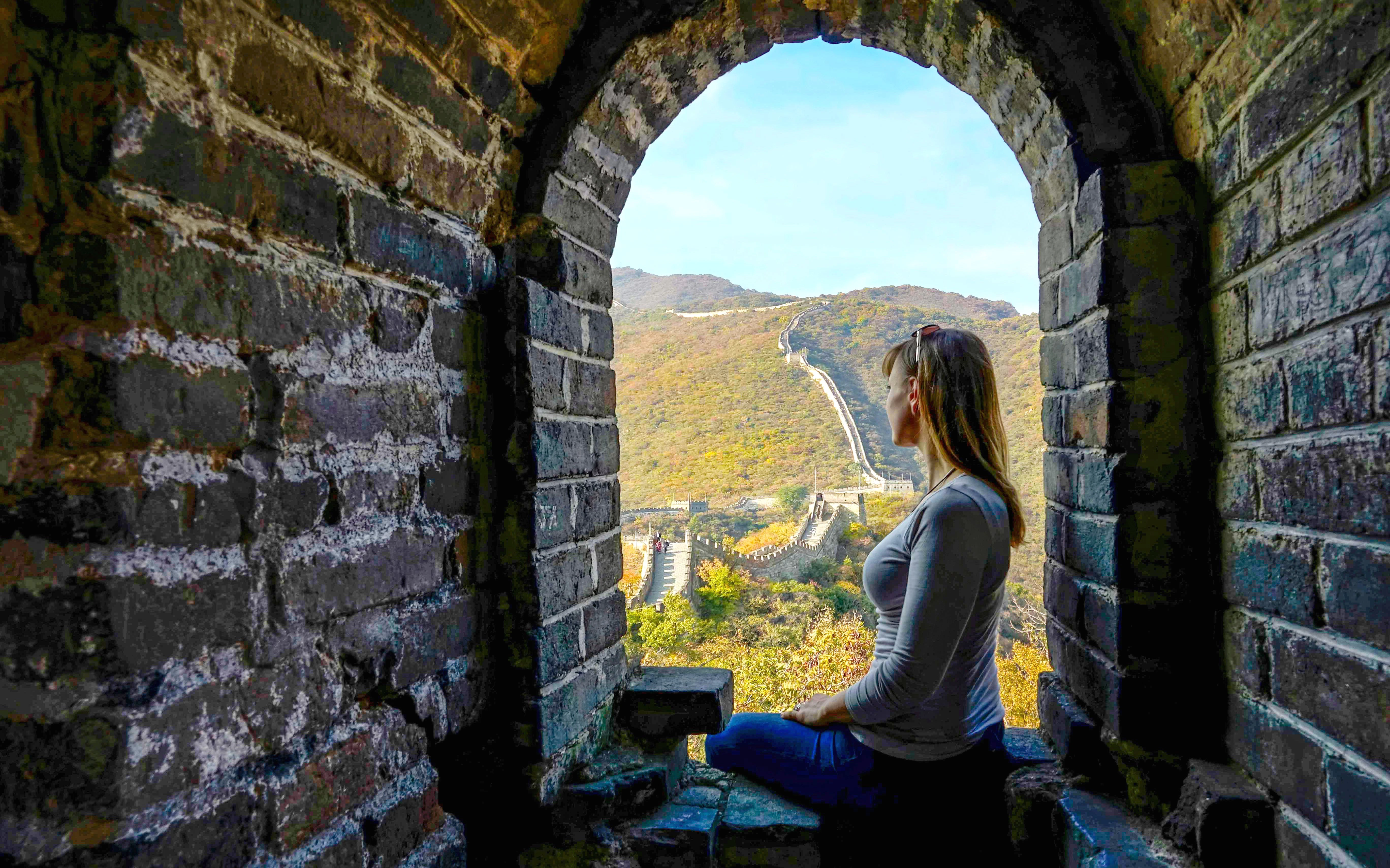 Woman sitting in window, viewing the Great Wall of China stretching over hills.