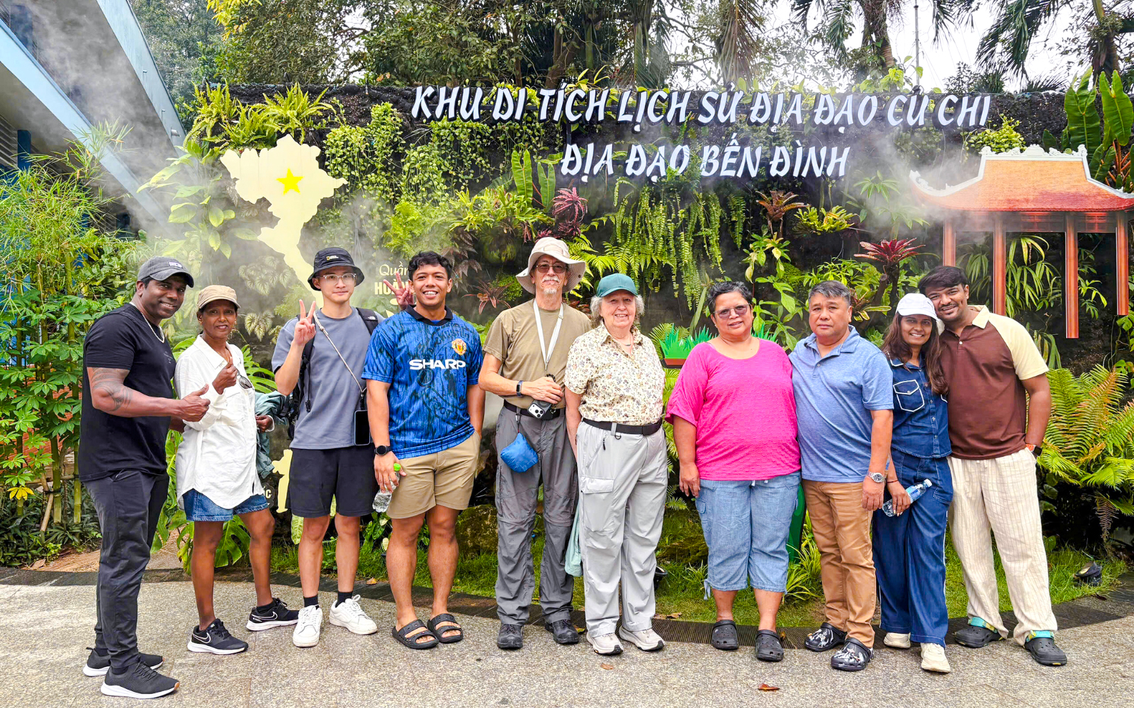Tourists posing at Cu Chi Tunnels entrance, Vietnam, with lush greenery and signage in the background.